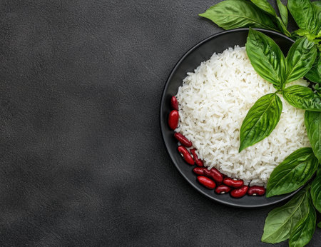 White rice with kidney beans and basil leaves on a black plateの素材