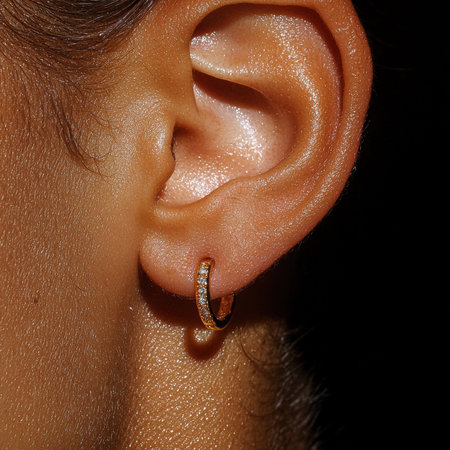 Close-up of a woman's ear with a gold hoop earring.の素材
