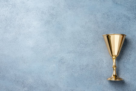 A shiny gold goblet on a textured blue background.の素材