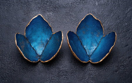 Two decorative blue and gold lotus flower bowls on a dark textured background.の素材