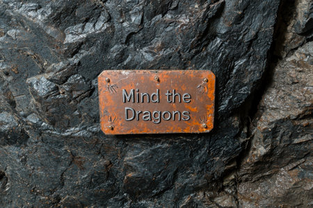 A weathered sign warns to mind the dragons on a rocky surface.の素材