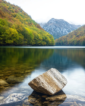 Scenic mountain lake with autumn foliage and a large rock in the foreground.の素材