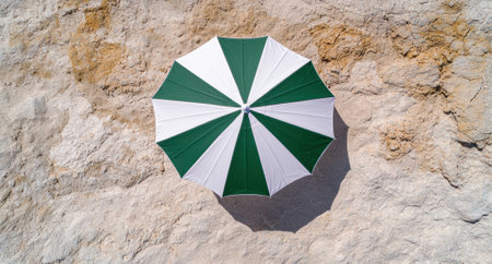 Green and white beach umbrella on a sandy surface.の素材