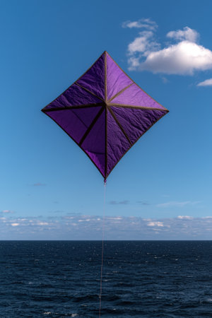Purple diamond kite flying over the ocean.の素材