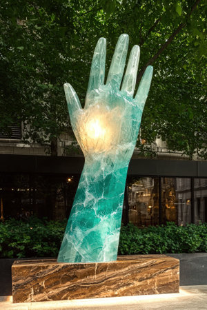 Illuminated crystal hand sculpture on a marble base outdoors.の素材
