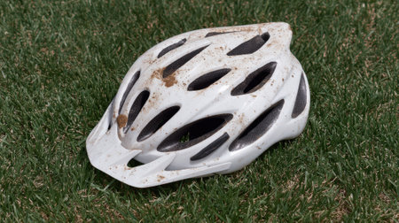 Muddy white bicycle helmet on green grass after accident.の素材