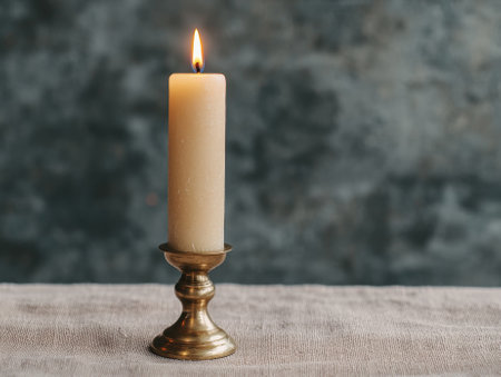 Elegant lit candle on a brass candlestick holder.の素材