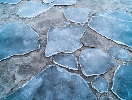 Cracked ice fragments on a concrete surface, winter scene.の素材