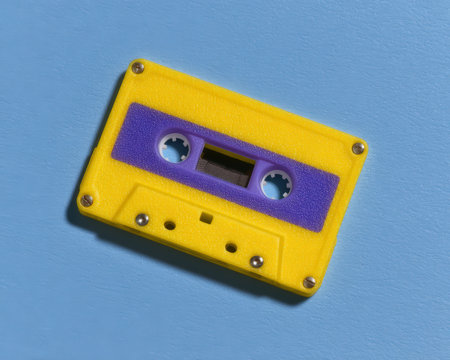 Vibrant yellow and purple audio cassette tape on blue.の素材