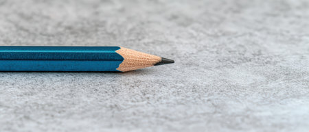 Sharpened blue pencil point on a textured gray surface.の素材