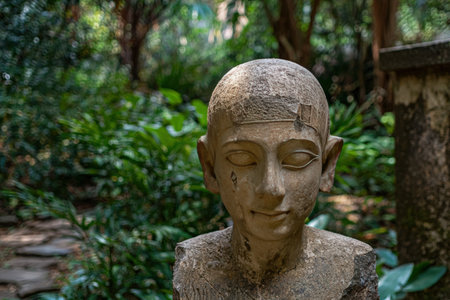 Ancient Egyptian bust statue in a lush garden setting.の素材