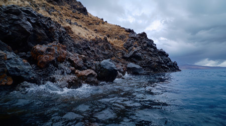 Waves crash against a rocky, grassy coastline under clouds.の素材