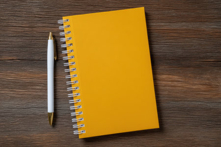 Yellow notebook and white pen on a wooden table.の素材