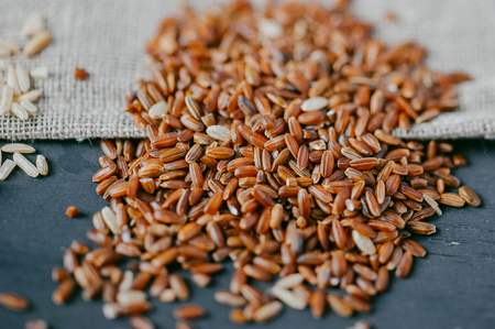 Heap of red Rice on black wooden background with burlap sackの写真素材