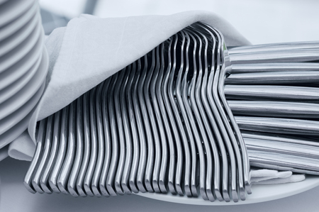 Elegant set of forks and knives silverware with napkin on white tablecloth with pile of platesの写真素材