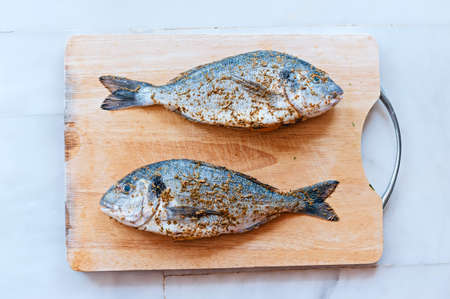 Two fresh dorado sea water fish with spices and salt on wooden cutting boardの写真素材