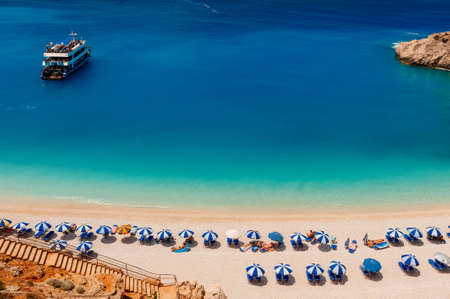 Mediterranean sea coastline top view with pleasure boat in green blue water and tourists on sandy shore under colorful umbrellasの写真素材