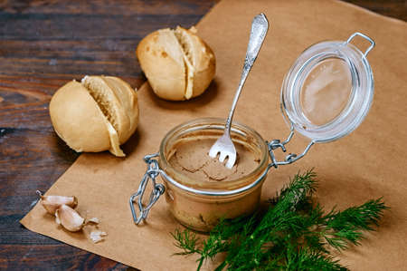 Prepared homemade French starter meal foie gras spread with white hot toasted buns and butter, cloves of garlic, green dill and spoon on wooden table rustic styleの写真素材
