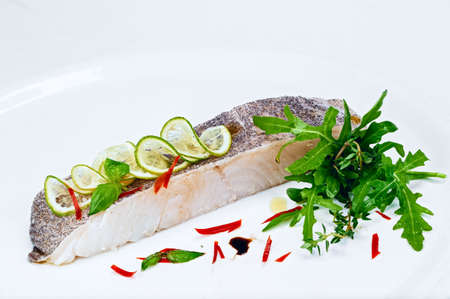 Grilled fillet of delicious white fish decorated with lemon slices and fresh green arugula salad...