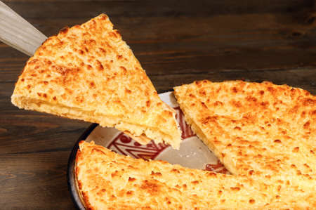 Segment of freshly cooked slice of cheese-filled pie on spatula and plate on wooden background