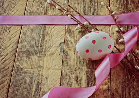 Easter background with egg, pink ribbon and willow branch on a wooden tableの写真素材