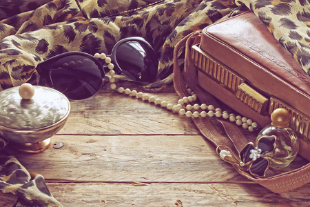 womens vintage accessories, powder box, scarf, necklace, sunglasses and handbag on wooden tableの写真素材