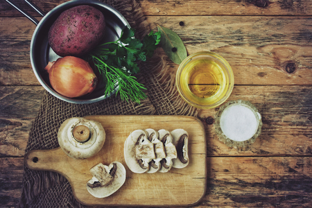 fresh raw sliced mushrooms with herbs, potato and onion on wooden plank with sackcloth napkin, top viewの写真素材