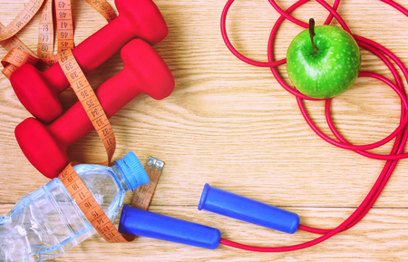 dumbbells, apple, bottle of water, measuring tape and skipping rope on wooden planks, fitness concept, top viewの写真素材