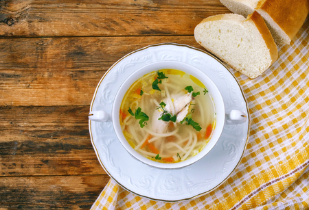 homemade chicken noodle soup,  napkin, bread on a wooden table, rustic style, top viewの写真素材