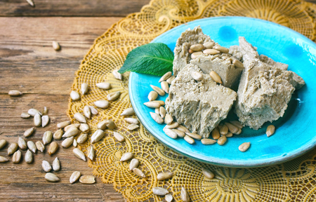 slices halva on turquoise ceramics plate, oriental sweets, sunflower seeds, mint leaves, lace napkin on a wooden tableの写真素材