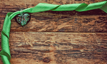 green heart with green silk ribbon on old wooden planksの写真素材