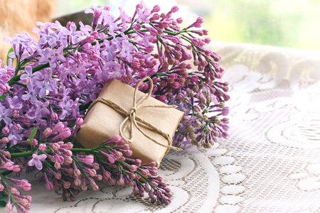 bouquet of violet lilac, small wrapped gift box on a table with tablecloth, about windowの写真素材