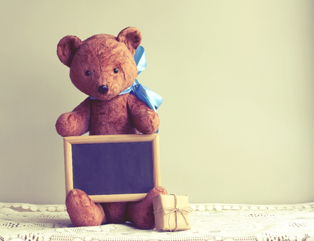 Old worn toy bear with blue bow, photo frame, gift box on table, retro tonedの写真素材