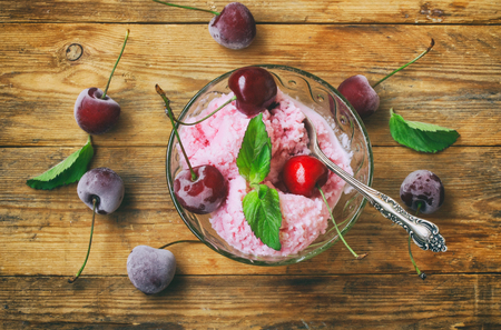 Homemade yogurt ice cream, with cherry, in glass bowl with spoon on wooden table, mint leaves, top viewの写真素材