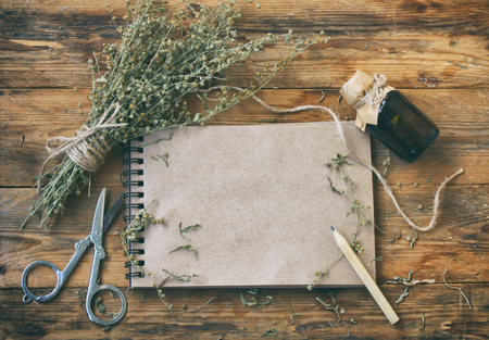 bunch of herb wormwood, jars of oil, scissors, notebook and pencil on an old wooden table, rustic style, vintageの写真素材