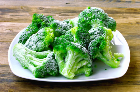 Fresh frozen broccoli on white plate, wooden table, healthy diet food, closeupの写真素材