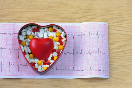 cardiogram, box of pills and heart on wooden table