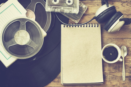 Retro music background, vinyl records, reel tape, cassette, headphones, cup of coffee and notebook on old wooden table, tonedの写真素材