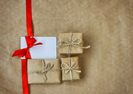Three gift box, white card with red ribbon bow on background of kraft paper