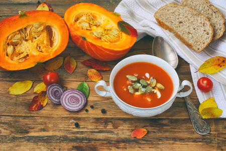 pumpkin soup puree in white bowl on wooden table, autumn leaves, rustic styleの写真素材