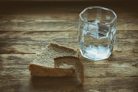 glass of water and hunk black bread crust on old wooden table, concept hunger need