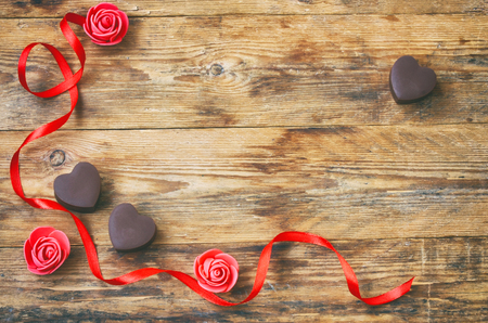 Valentine`s Day greeting card, milk chocolate heart shape, rose, red satin ribbon on a wooden tableの写真素材