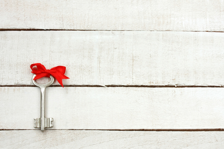 key with red bow silk ribbon, on white wooden table, free space for textの写真素材