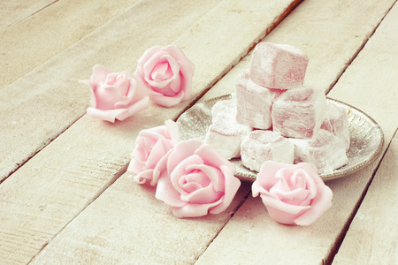 Turkish delight with rose flavor in metal plate, pink roses flowers on wooden tableの写真素材