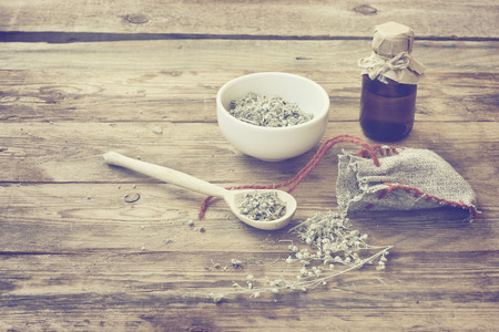 homemade sachet with wormwood, white bowl with dry herb, bottle of oil on wooden table, monochrome sepia photo, vintage styleの写真素材