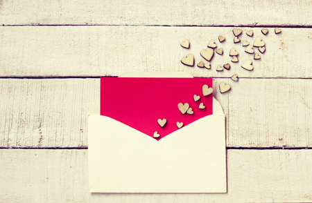 Valentine's day congratulation card,  bunch of different plywood hearts on  white wooden table, envelope with empty red texture paperの写真素材