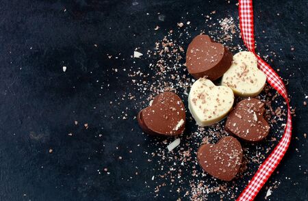 Valentines day background, home made chocolate dark and white hearts and ribbon, on black shabby surfaseの写真素材