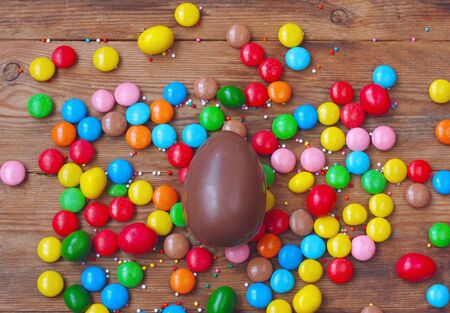 Easter chocolate egg, colorful candy on wooden table. Delicious dessert holiday food, top viewの写真素材