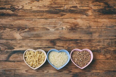rice, pasta, buckwheat, in bowl  heart shape, grocery products on wooden table, top view, space for...