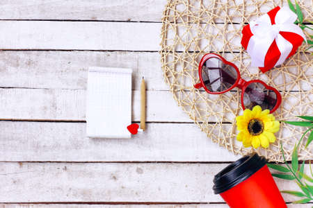 red sunglasses heart shape, coffee, yellow flower, notebook with pencil on white wooden table, top view, mock upの写真素材